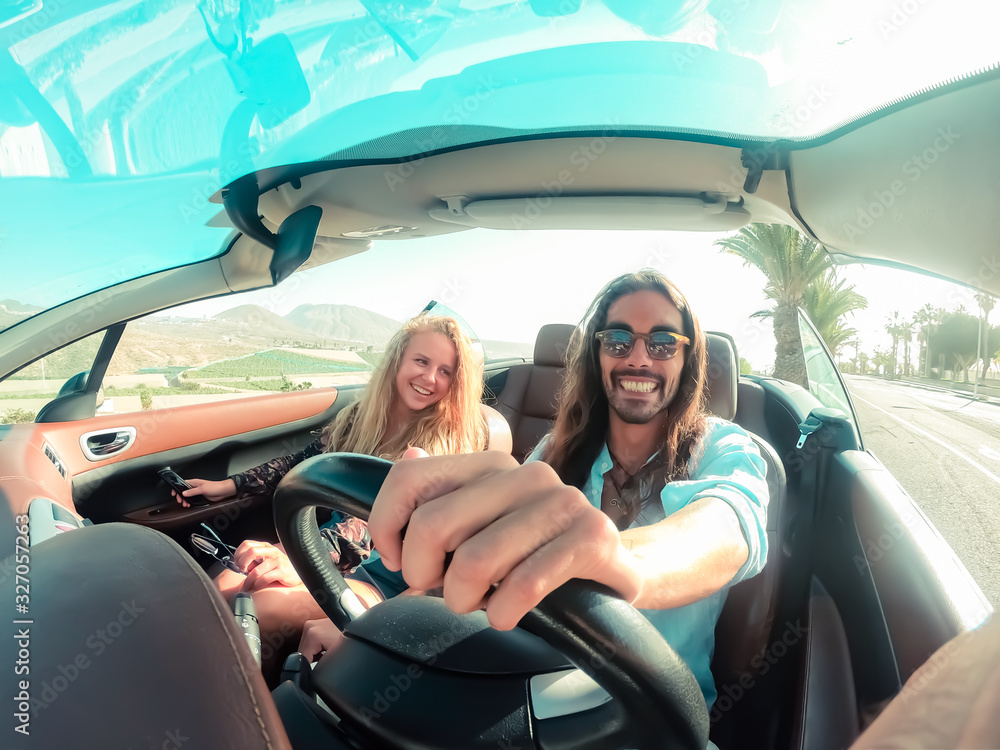 Happy young couple having fun during road trip in convertible car. Romantic lovers enjoying time together driving cabriolet auto in luxury vacation in a tropical city. Vacation, journey and relationsh