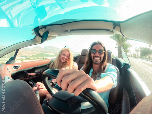 Happy young couple having fun during road trip in convertible car. Romantic lovers enjoying time together driving cabriolet auto in luxury vacation in a tropical city. Vacation, journey and relationsh photo