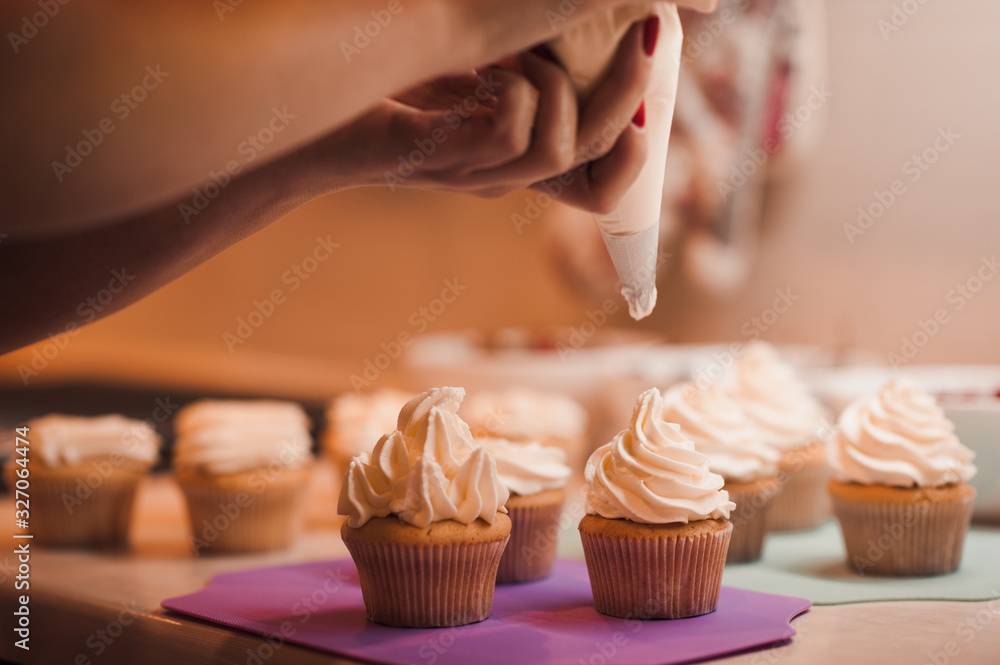Woman decorating cupcakes with cream cheese on kitchen table closeup. Preparing for birthday party.