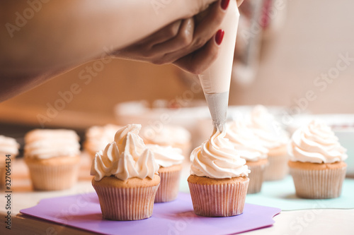 Woman making icing on cupcakes with cream cheese on kitchen table closeup. Preparing for birthday party. photo