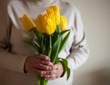 hands of an elderly woman holding a bouquet of yellow tulips