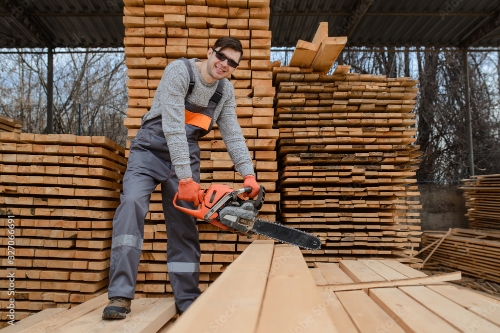 A portrait of young man carpenter at the wooden warehouse hold in his hands a chainsaw A portrait of young man carpenter at the wooden warehouse hold in his hands a chainsaw