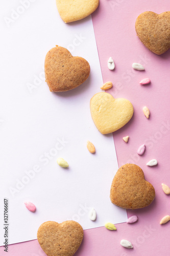 Heart shaped cookies and colorful sprinkles with shirt of paper, copy space for text. Pink paper background. Love concept, 8 March, International Happy Women's Day, Birthday.