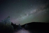 USA, Nevada, Nye County, West Stone Cabin Valley. A surreal night sky Milky Way Galaxy scene with a purple and green hue above Knoll Spring Dirt Road lit by headlights
