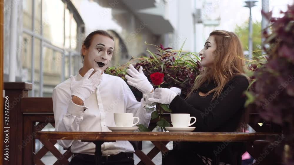 Two happy mime on a date in the cafe. Happy man giving a flower to his girlfriend. Romantic date Two happy mime on a date in the cafe. Happy man giving a flower to his girlfriend. Romantic date