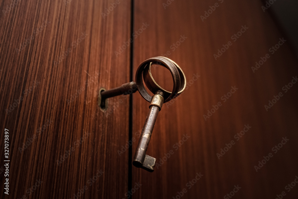 Couple of old bronze keys on a keyhole of a wooden door Couple of old bronze keys on a keyhole of a wooden door