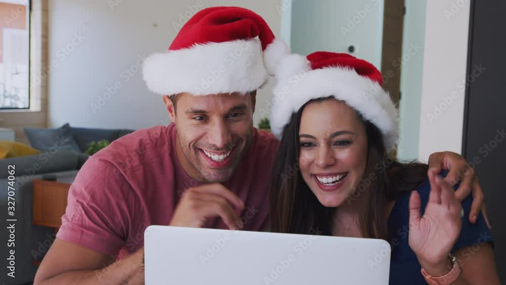 Hispanic Couple Wearing Santa Hats With Laptop Having Video Chat With Family At Christmas Hispanic Couple Wearing Santa Hats With Laptop Having Video Chat With Family At Christmas