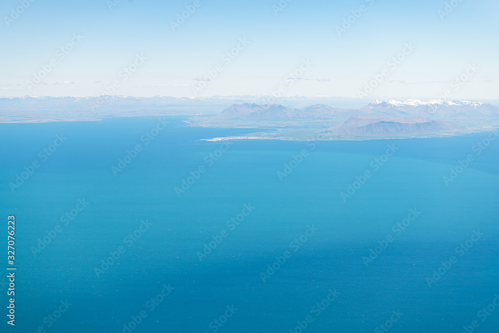 Fototapeta premium Keflavik, Iceland airport with aerial high angle view of Reykjavik city from airplane window above and colorful ocean water