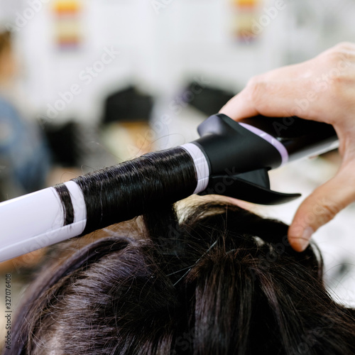 Hairstylist curling hair close up. Hairdresser making hairstyle to brown long hair woman in beauty salon. Professional hair care, Hairdressing services. Hair styling process.