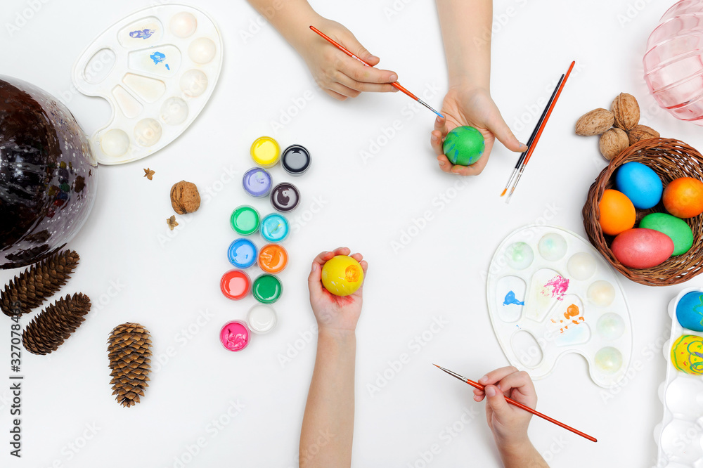 Joint traditional coloring of the symbol of Easter. Hands, brushes, paints, palette, eggs on a white background Joint traditional coloring of the symbol of Easter. Hands, brushes, paints, palette, eggs on a white background