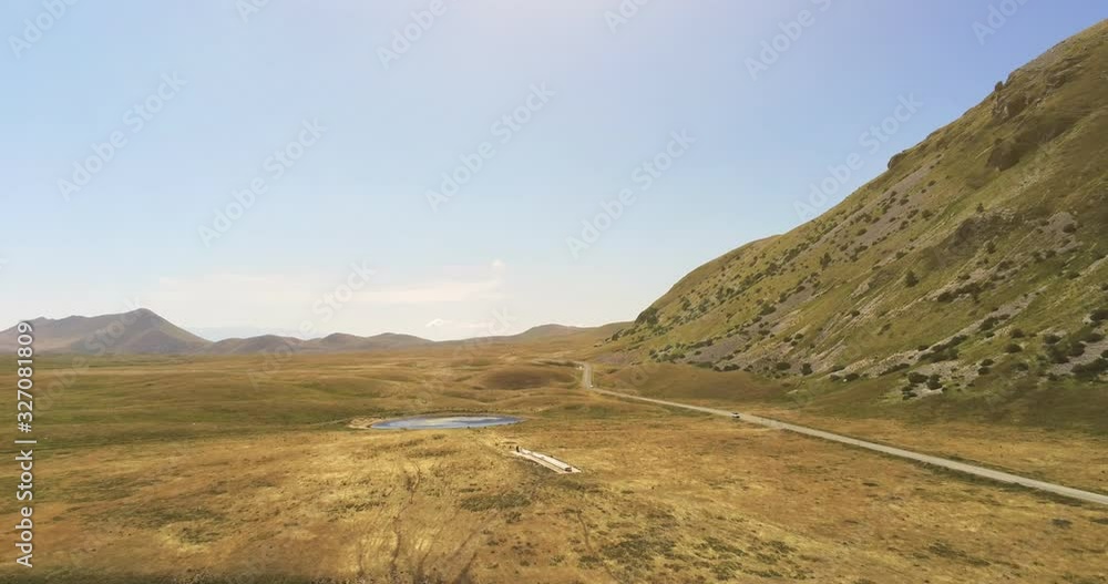 Aerial top view dolly in shot of a gorgeous mountain landscape with bare ground in a yellow highland flat land near the big mountain of Gran Sasso, Campo Imperatore, Abruzzo, Italy. Aerial top view dolly in shot of a gorgeous mountain landscape with bare ground in a yellow highland flat land near the big mountain of Gran Sasso, Campo Imperatore, Abruzzo, Italy.