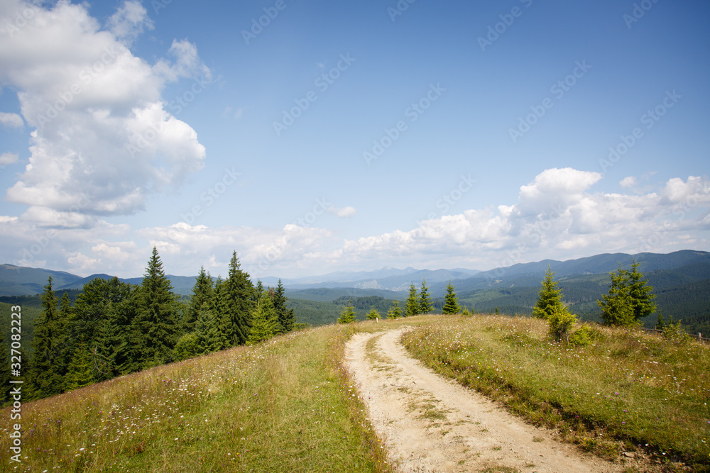 Carpathian landscape. Dirt road in the mountains. Hiking. Rural landscape in Carpatians, Ukraine. Coniferous forest and beautiful sky. Wooden fence. Panorama of mountains from Mount Kostrycha, Ukraine