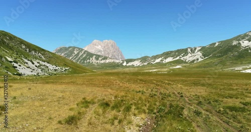 Aerial top view shot of a gorgeous mountain landscape with bare ground in a yellow highland flat land near the big mountain of Gran Sasso, Campo Imperatore, Abruzzo, Italy.
