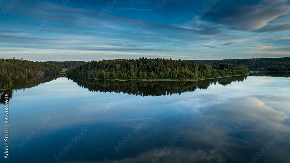 Reflection of the blue sky and green forest in the calm water of the lake.