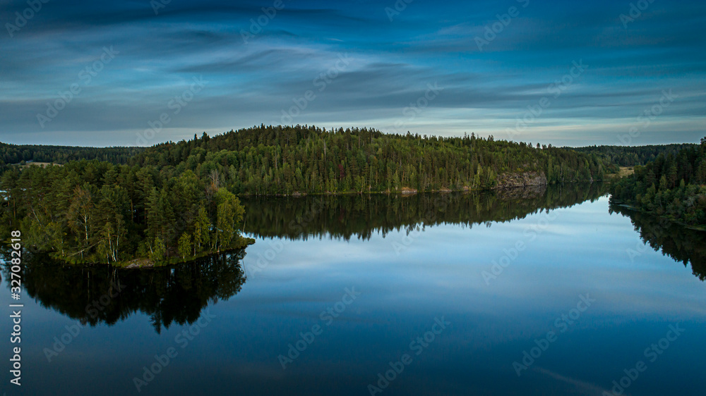 Reflection of the blue sky and green forest in the calm water of the lake.