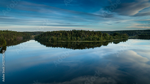 Reflection of the blue sky and green forest in the calm water of the lake.