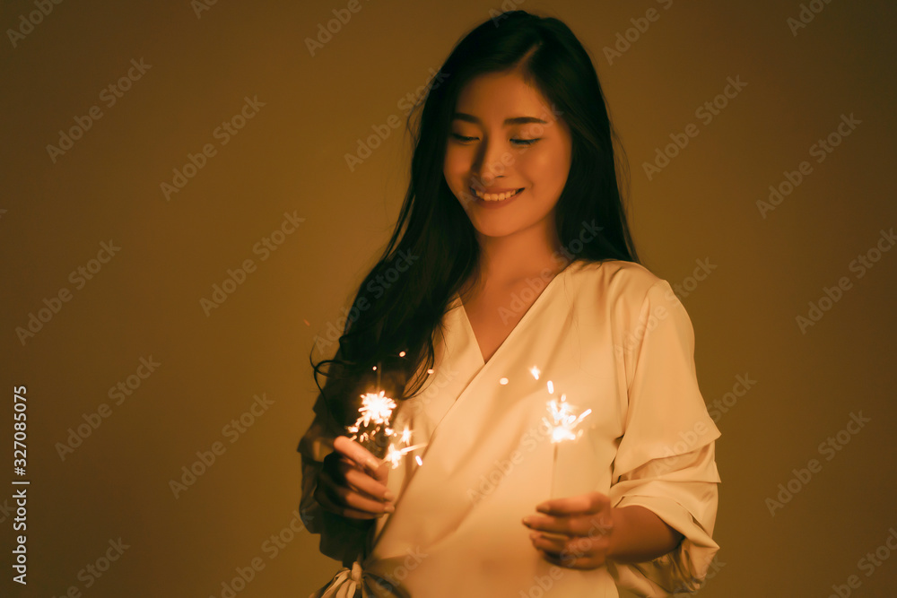 Asian woman holding bright festive Christmas sparkler in hand,firework pyrotechnics and bokeh on the dark background for celebration concept