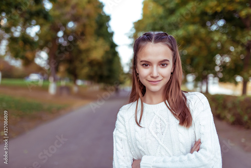 Portrait of a teenage girl of 12 years old, in summer in park, casual clothes, white knitted sweater, free space for copy text. Weekend break. Emotions of happiness are smiles and positive.
