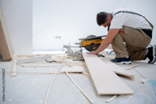 Man cutting laminate floor plank with electrical circular saw