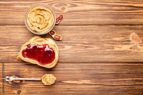 Toast sandwich with peanut butter. Spoon and jar of peanut butter, jam and peanuts for cooking breakfast on a brown wooden background. Creamy peanut paste flat lay with place for text.