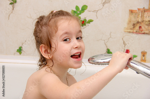 The little girl holds a shower in her hands and pours herself water.
