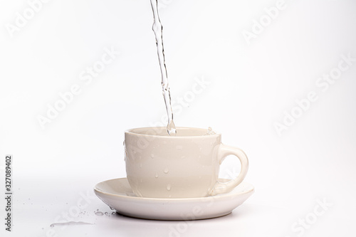 High speed studio photograph of water pouring and splashing into a white mug, isolated against a plain white background