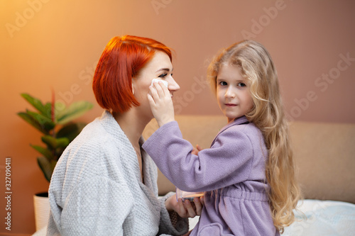 Daughter makes mom make up at home on bed.