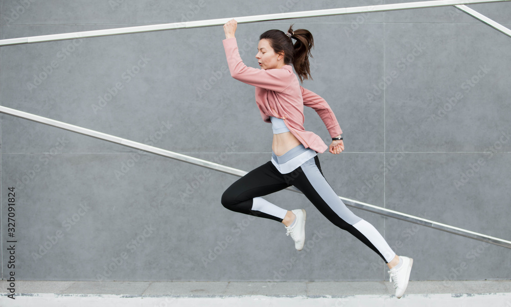 An athletic young woman is jumping, doing acrobatics, ballet, is actively involved in sports, against a concrete wall.