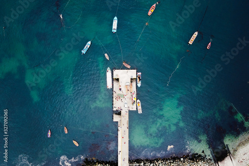 Aerial view of fishermen pier dock with many fishing boats parked in a harbour. Green and blue colors of Pacific ocean. Bird's eye view from above of small fishing port. Bahia Mansa, Osorno, Chile.