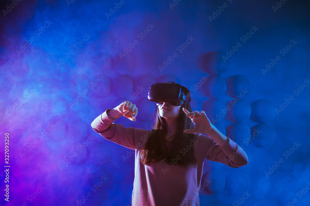 A delighted young woman in virtual reality glasses, against the futuristic background get experience in virtual space. A delighted young woman in virtual reality glasses, against the futuristic background get experience in virtual space.