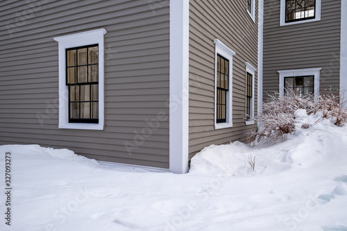 A tan colored vintage wooden building with multiple windows. The exterior walls are covered in narrow clapboards and wide white corner boards. There's a drift of snow in front of the building.  © Dolores  Harvey