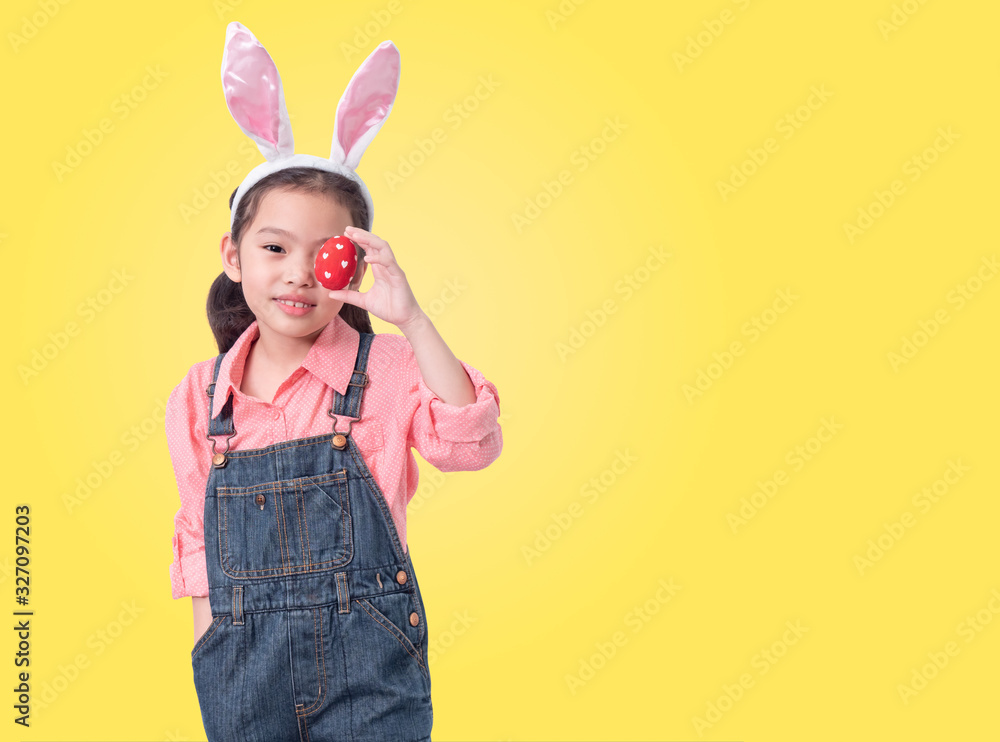 Happy little cute girl 6 years old wearing rabbit ears and holding red easter eggs close her eye on yellow background with clipping part.