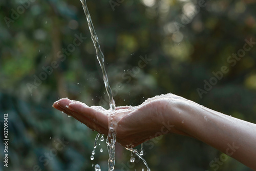 Water pouring on hand with blurred nature background.