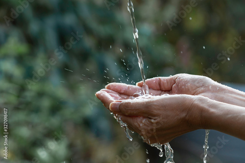 Water pouring on hand with blurred nature background.
