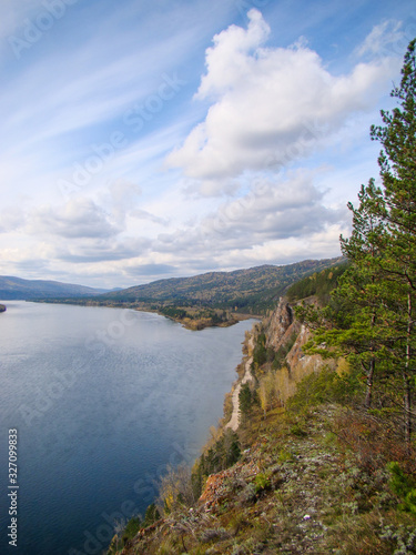 Steep bank of a large river. Blue water, forest, road, sky. Vertical layout. Concept of tourism, vacation, ecology.