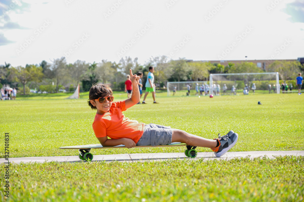 young boy lying skateboard pointing up suntan sidewalk smiling soccer field love life grateful