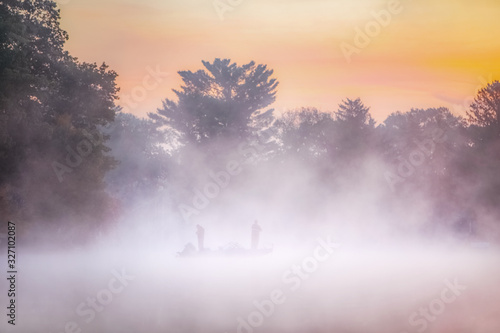 Soft misty image of fishermen standing in a boat on a lake in early morning dense fog