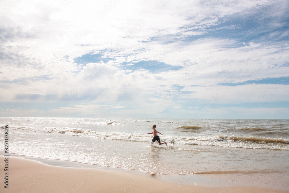 Boy running on beach splashing in the waves