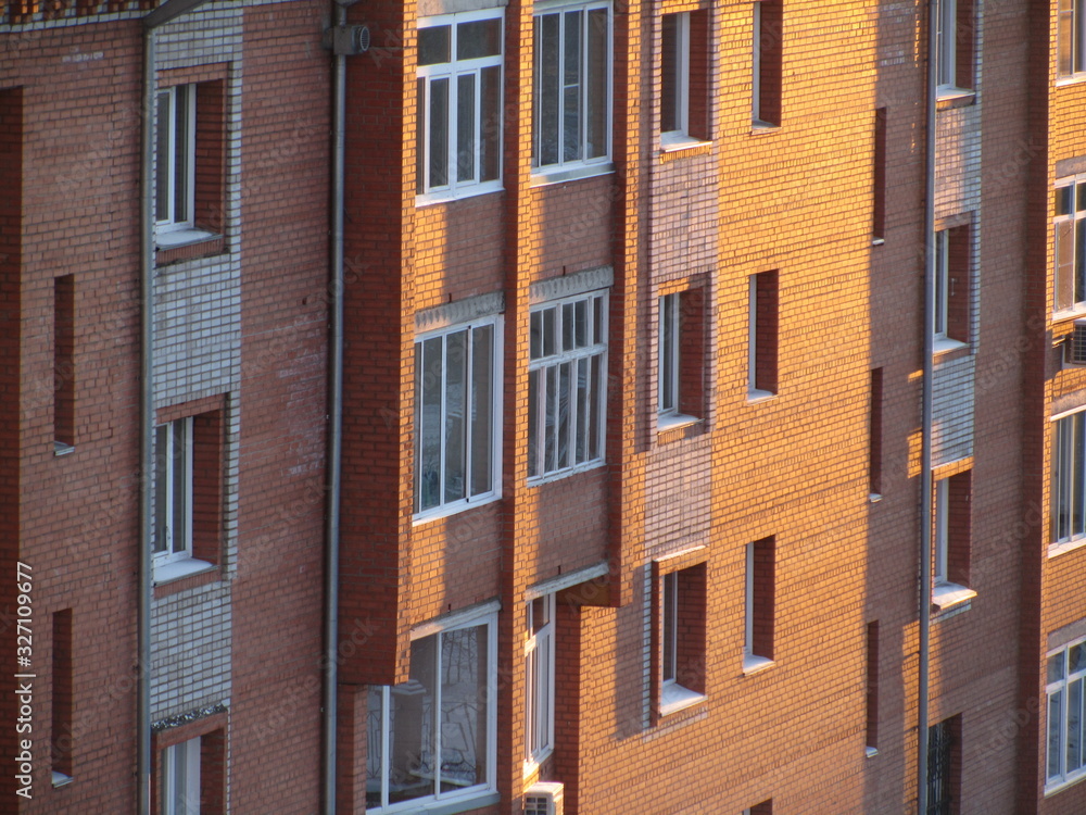 Modern brick residential building close-up. Perspective view of a house wall with windows and balconies. Facade of a brick urban apartment building. Modern brick residential building close-up. Perspective view of a house wall with windows and balconies. Facade of a brick urban apartment building.