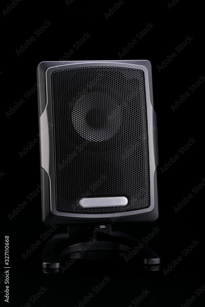 A small, black audio speaker for a computer, on a black background. A small, black audio speaker for a computer, on a black background.