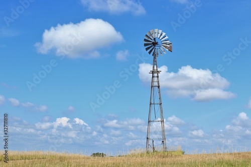 Kansas Country Windmill with green grass and blue sky with clouds in Kansas.