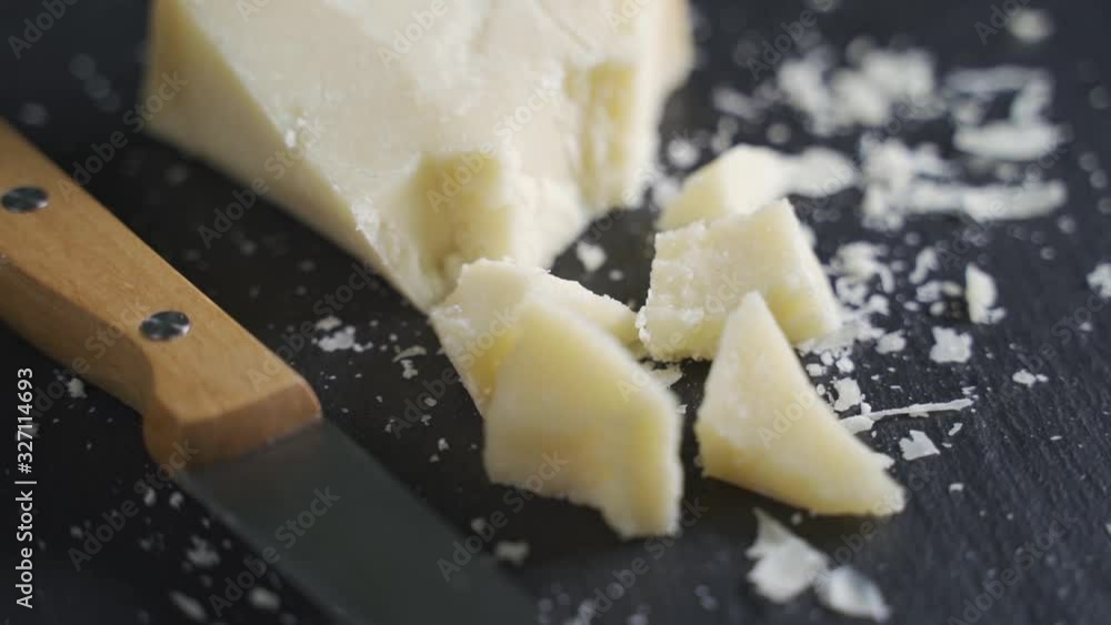 Hard gourmet parmesan cheese on a black stone plate. Plate rotates, close-up Hard gourmet parmesan cheese on a black stone plate. Plate rotates, close-up