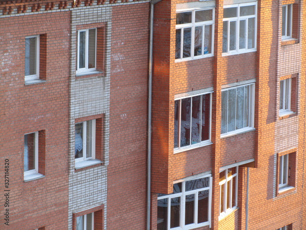 Modern brick residential building close-up. Perspective view of a house wall with windows and balconies. Facade of a brick urban apartment building. Modern brick residential building close-up. Perspective view of a house wall with windows and balconies. Facade of a brick urban apartment building.