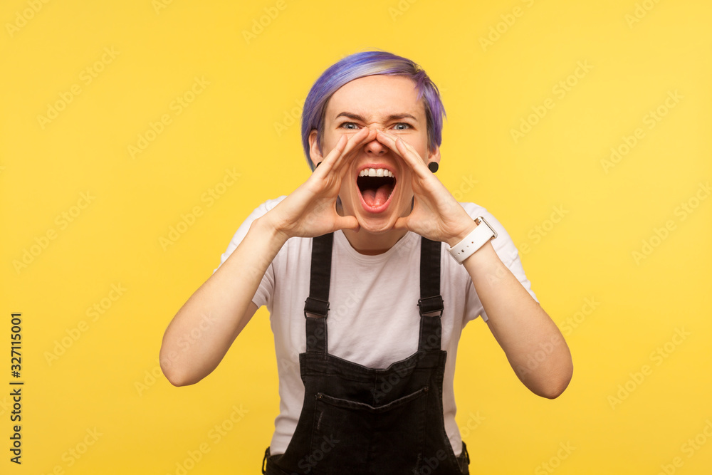 Attention! Portrait of hipster girl with violet short hair in denim overalls screaming emotionally and loudly negative announcement at camera, crazy news. isolated on yellow background, studio shot Attention! Portrait of hipster girl with violet short hair in denim overalls screaming emotionally and loudly negative announcement at camera, crazy news. isolated on yellow background, studio shot