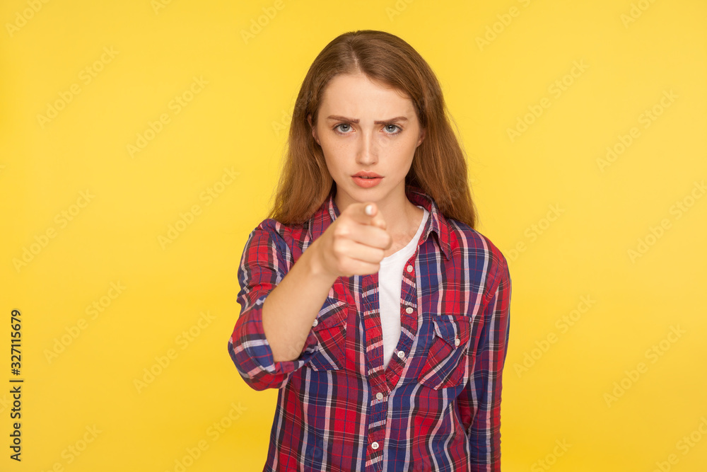 Hey you! Portrait of serious displeased ginger girl in checkered shirt pointing finger at camera and accusing blaming with bossy expression, strict warning. studio shot isolated on yellow background Hey you! Portrait of serious displeased ginger girl in checkered shirt pointing finger at camera and accusing blaming with bossy expression, strict warning. studio shot isolated on yellow background