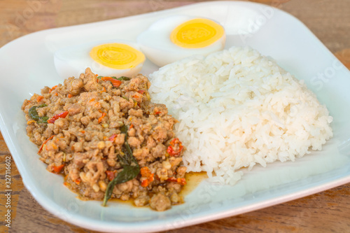 Close-up rice with stir-fried pork and basil served with boiled egg on white plate. Thai street food dishes.