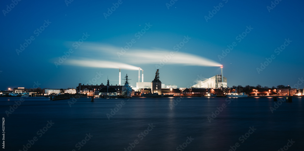 Old port crane with the working factory background at night in Copenhagen, Denmark. Larsens Plads Amaliekaj famous quay near Nyhavn. long exposure lights & clear sky with stars. Old European buildings