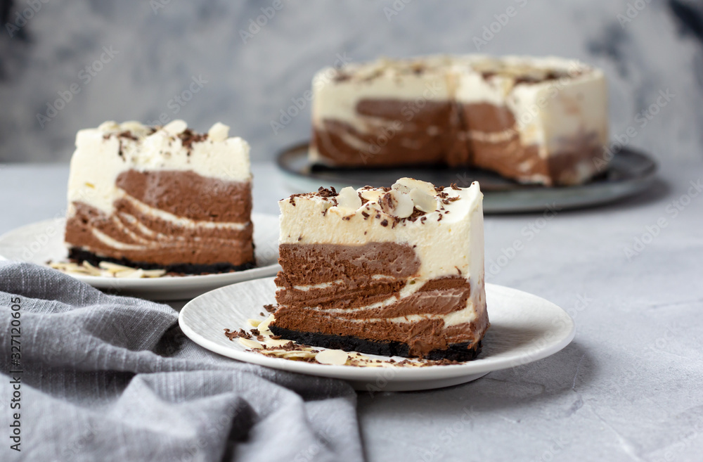 Pieces of homemade raw chocolate cheesecake or mousse cake decorated with almond flakes and chocolate chips on white plates. Horizontal orientation Pieces of homemade raw chocolate cheesecake or mousse cake decorated with almond flakes and chocolate chips on white plates. Horizontal orientation