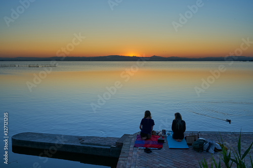 two women doing yoga on a pier at sunset                              