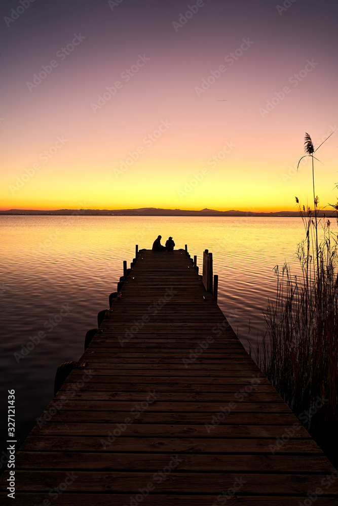 a couple on a pier watching the sunset on a lake                              